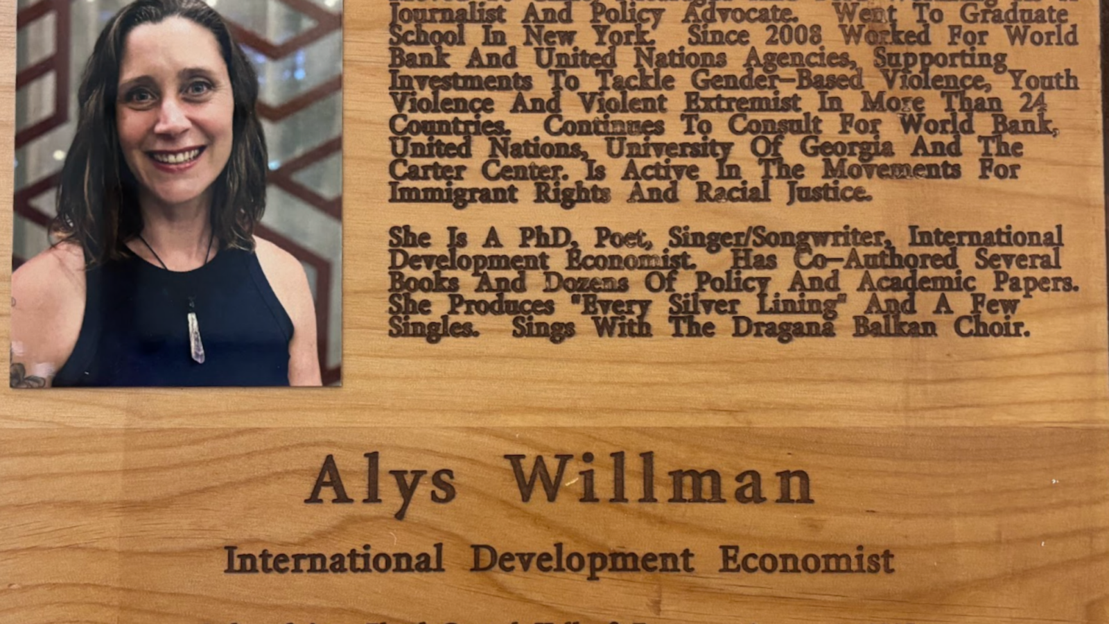 Wooden plaque with a photo of a smiling woman on the left and a biography block on the right describing her education and advocacy work.