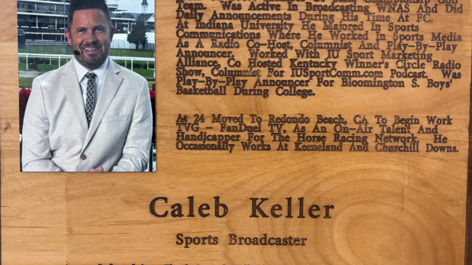 Wooden plaque featuring a portrait of a man in a light suit on the left and engraved biography text on the right.